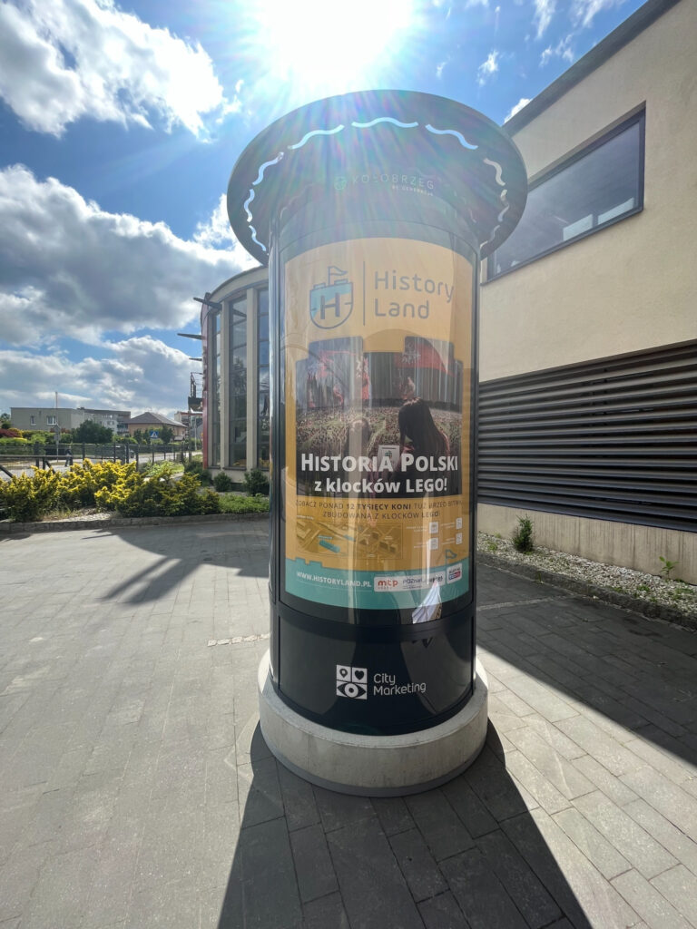 Słup reklamowy stojący na chodniku przed budynkiem